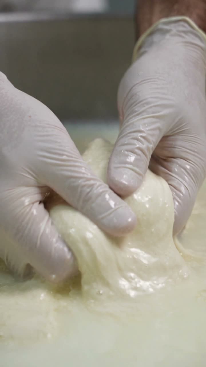 Hands stretching fresh curd into mozzarella